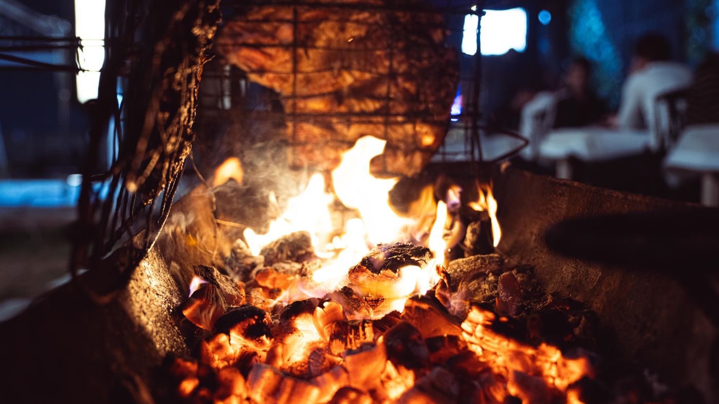 Carne cocinándose junto al fuego y las brasas de leña